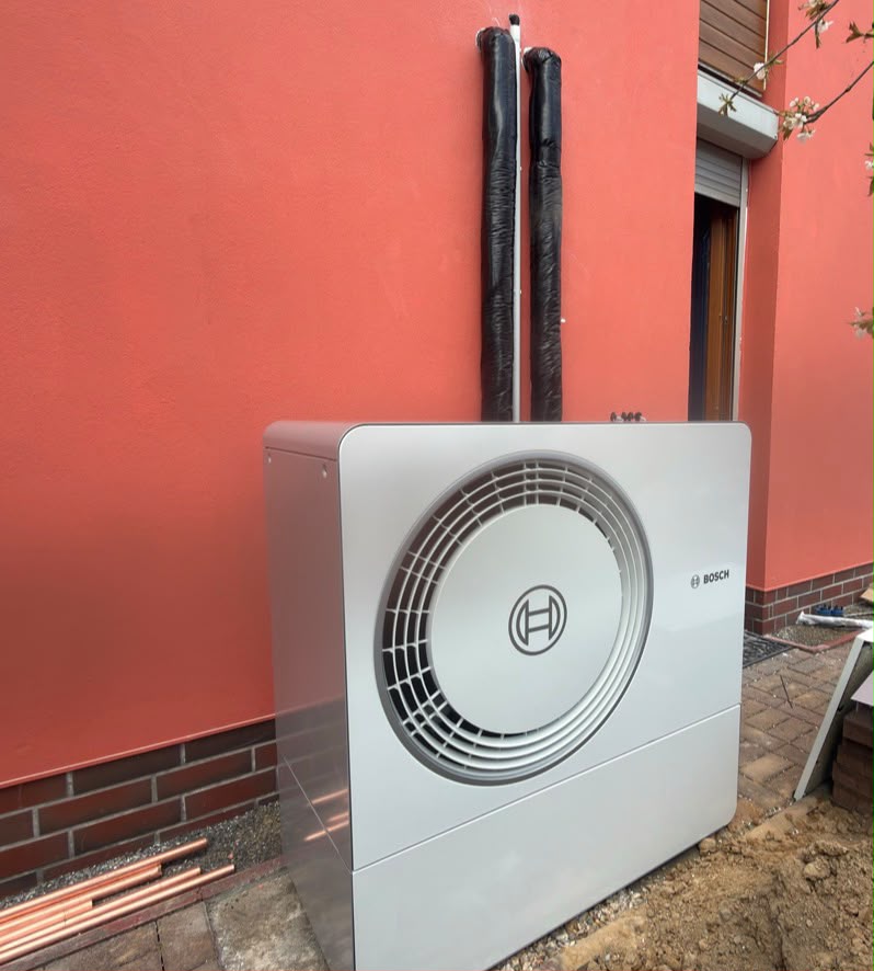 Außeneinheit einer Wärmepumpe an einer Hauswand mit angeschlossenen Leitungen